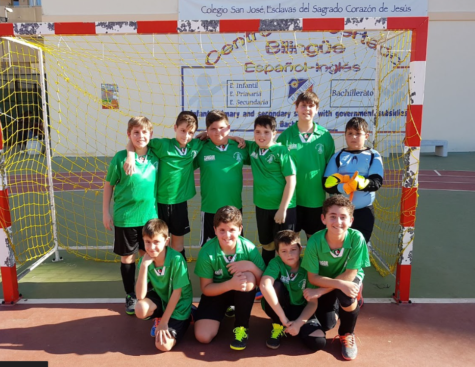 Equipo de fútbol infantil posando juntos frente a la portería en el colegio.
